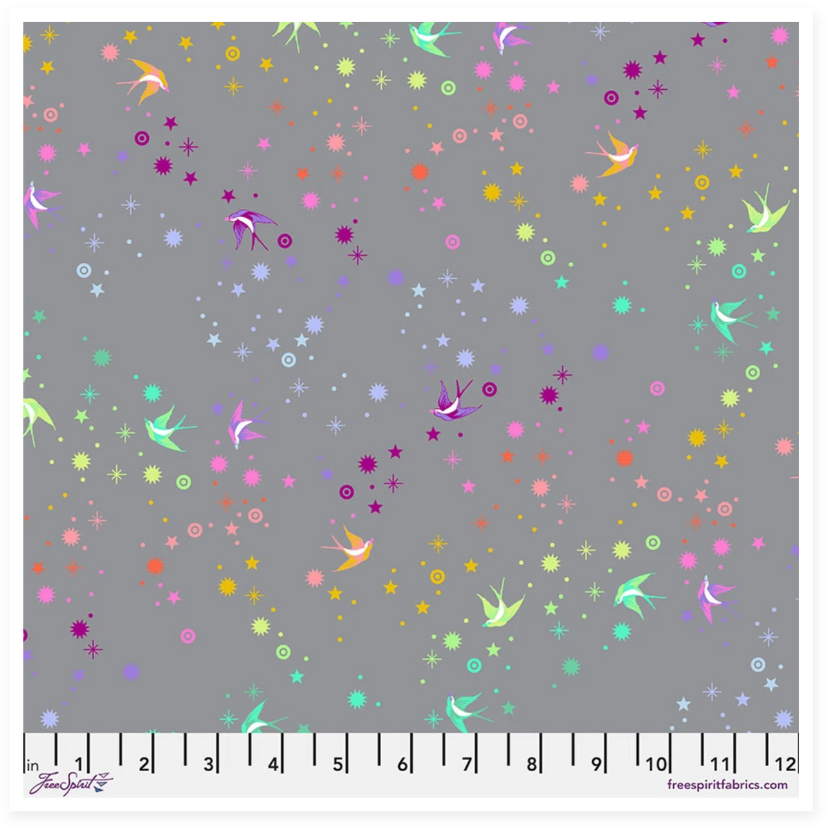 A fabric swatch preview for 'Fairy Dust - Shadow || Graywork' by Spring + Studio, showing a gray fabric base with scattered pastel and bright fairy-like motifs, stars, dots, and small birds. The right side includes product text and a ruler scale along the bottom.