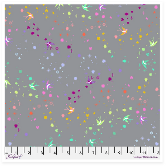 A fabric swatch preview for 'Fairy Dust - Shadow || Graywork' by Spring + Studio, showing a gray fabric base with scattered pastel and bright fairy-like motifs, stars, dots, and small birds. The right side includes product text and a ruler scale along the bottom.